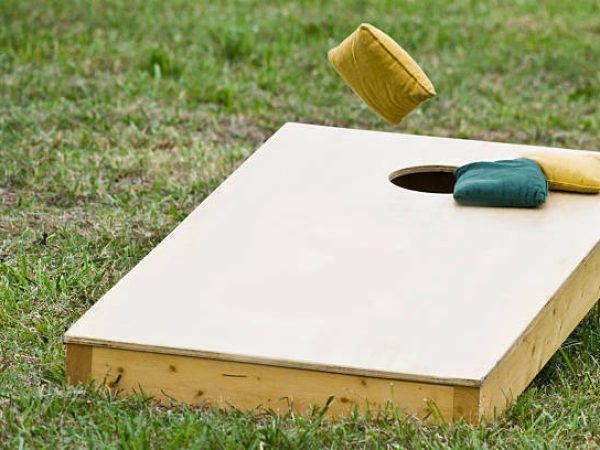 Cornhole board with bags and board being tossed